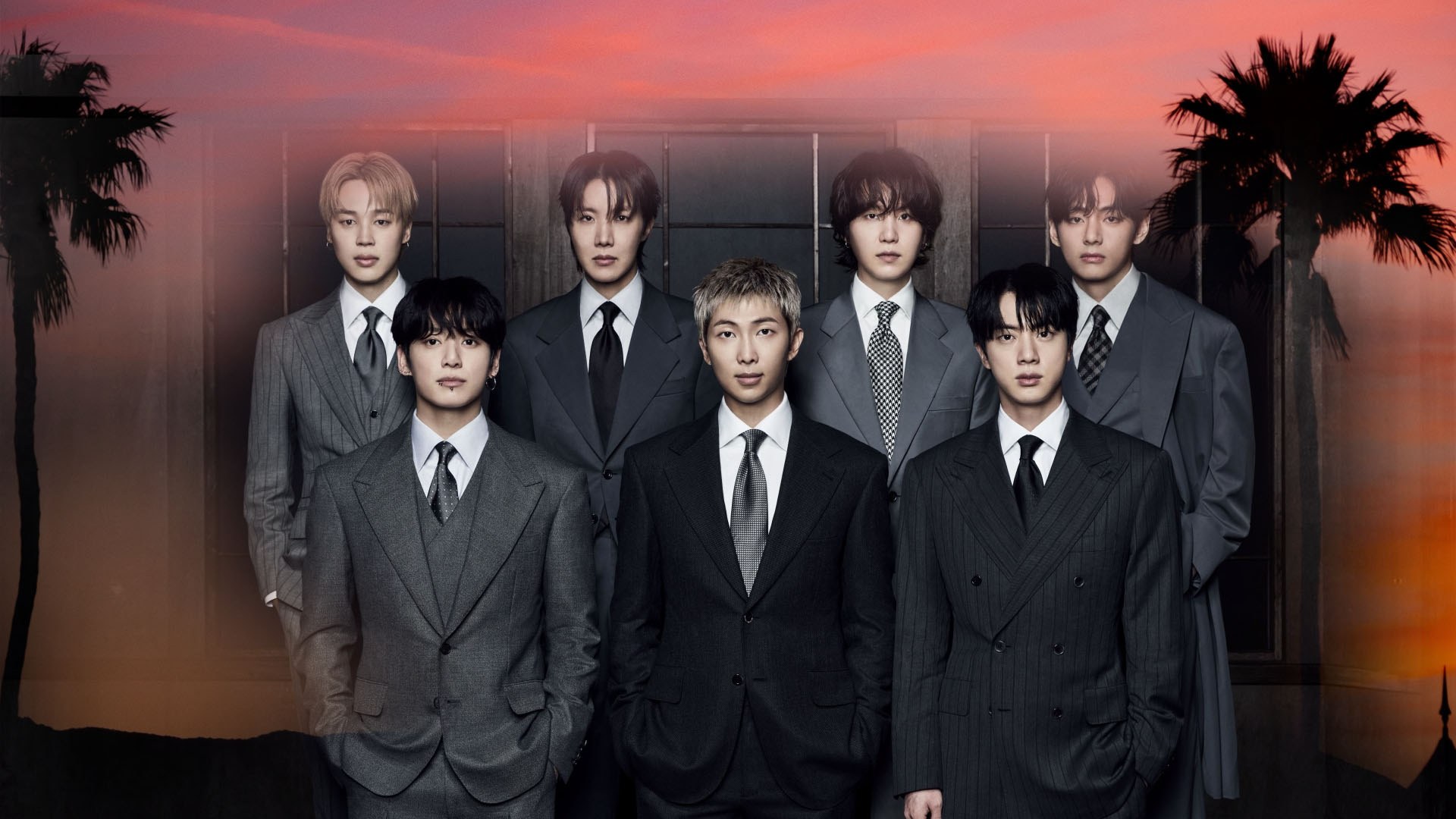BTS en trajes formales posando frente a un atardecer enmarcado por palmeras.