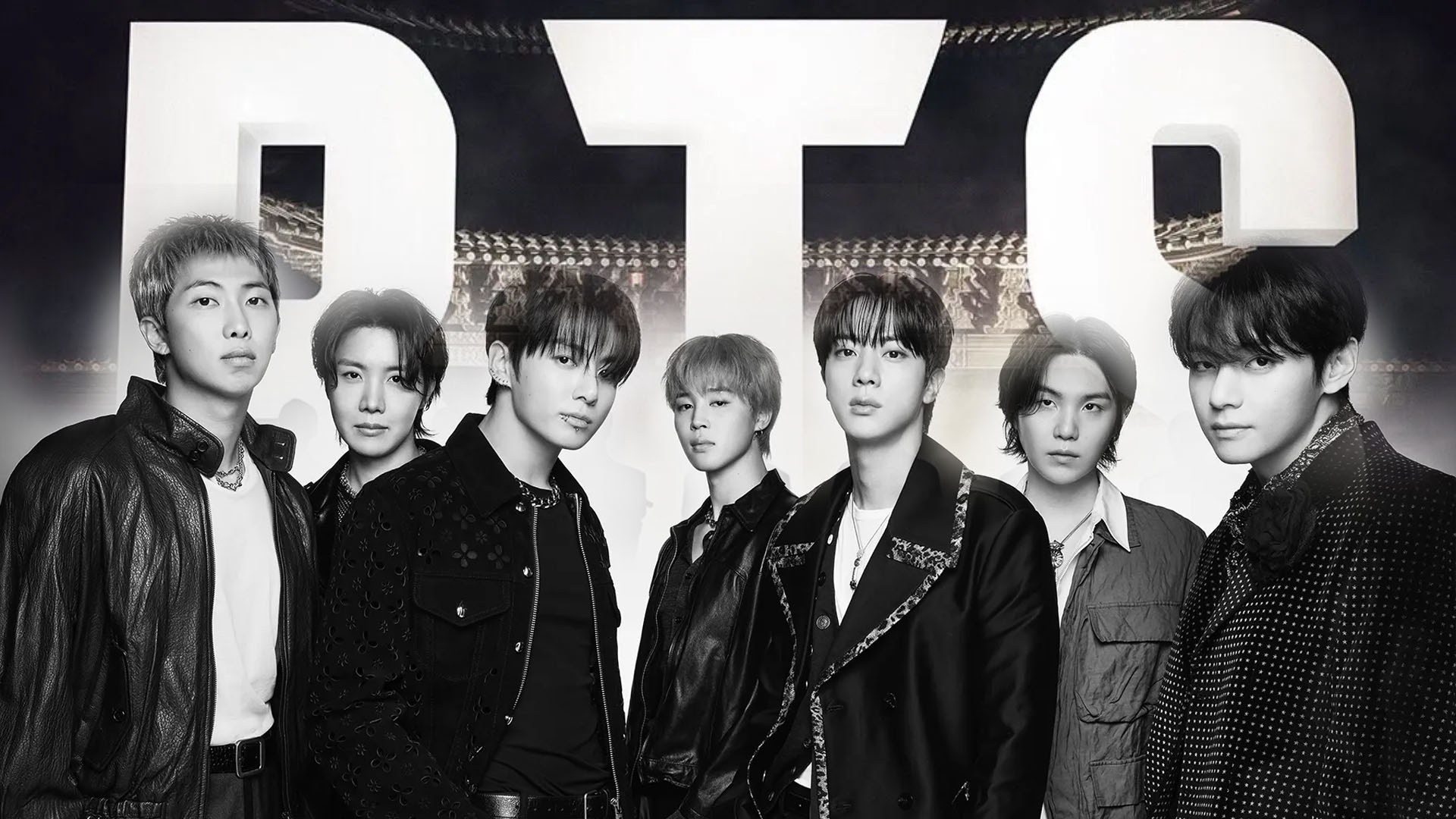BTS в тёмной коже и строгих пиджаках стоят плечом к плечу перед огромными белыми буквами BTS, чёрно-белое фото.