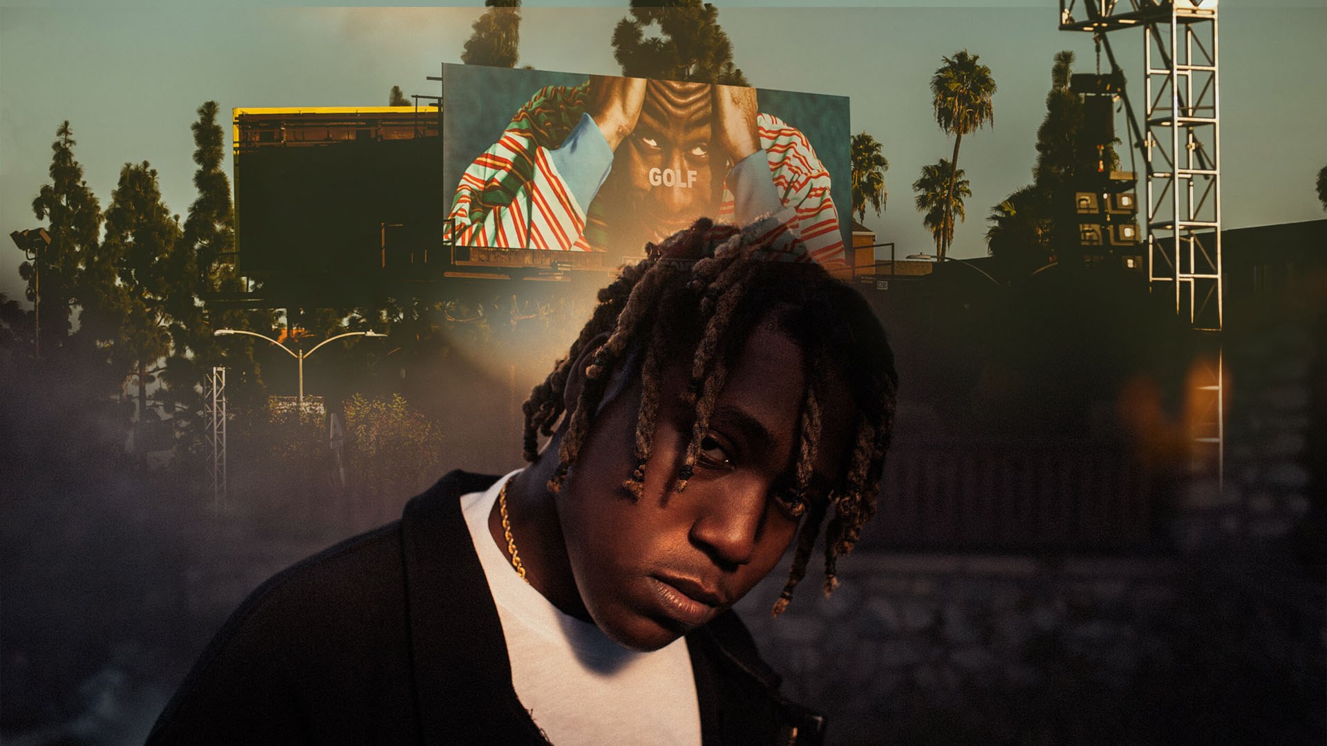 Don Toliver with braids in black jacket at outdoor festival with large stage screens behind him.