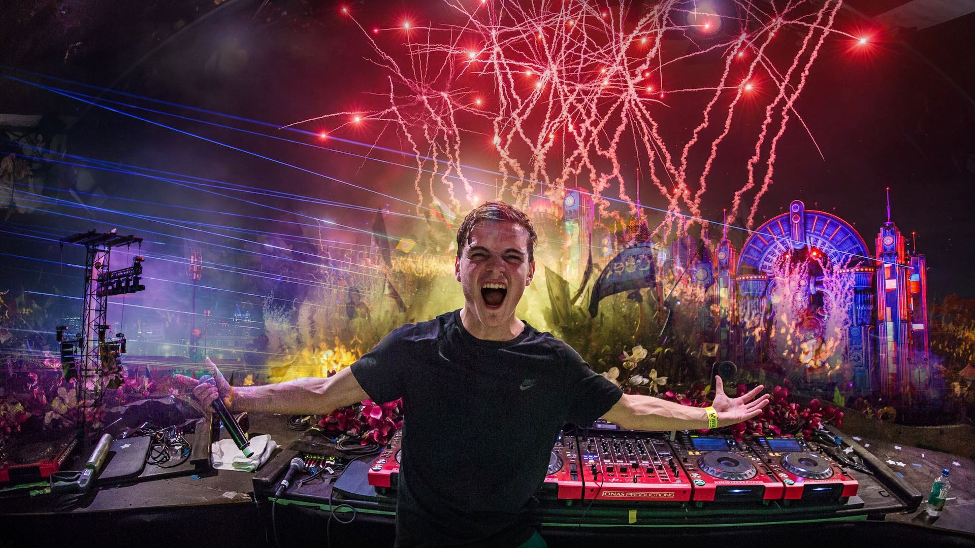 Martin Garrix energetically DJing at a festival stage surrounded by neon lights and pyrotechnics.