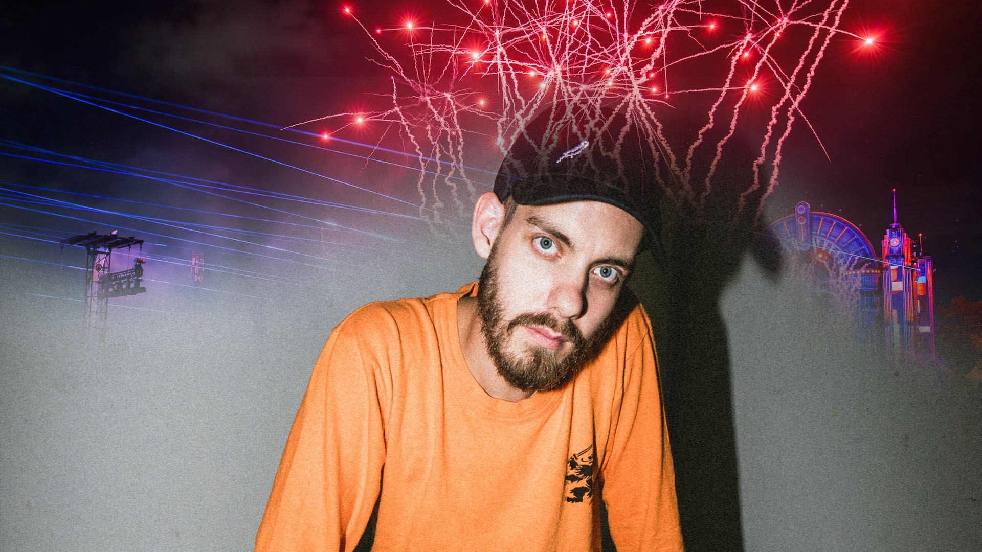 San Holo in a black cap and orange shirt leans forward under red fireworks, with lasers and neon rides at night.