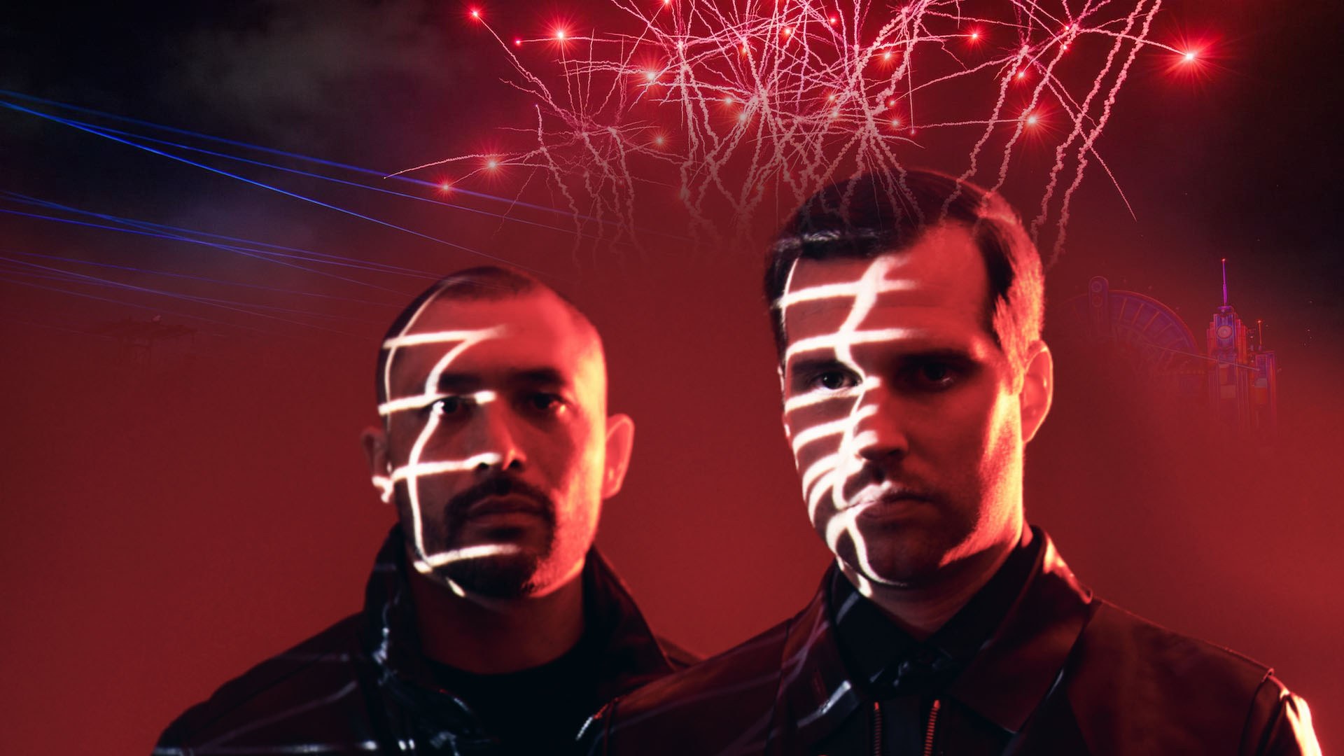 Two men in dark jackets stand under red light with white grid patterns on their faces and sparks bursting overhead.