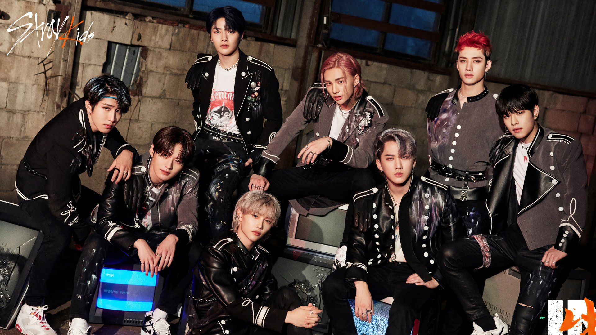 Stray Kids group promotional photo — all eight members posing together in black and gray leather fashion in an industrial warehouse setting