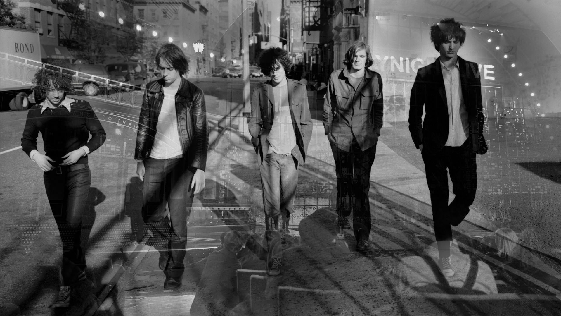 Five young men in jackets and jeans walk down a black-and-white city street past a partial "Saturday Night Live" sign.